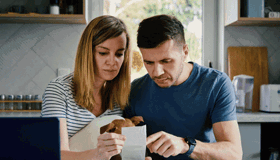 Couple Budgeting Sat At Table Looking At Receipt Landscape