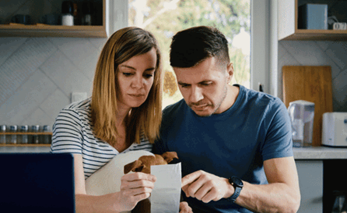 Couple Budgeting Sat At Table Looking At Receipt Landscape
