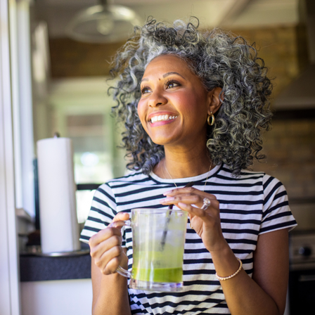 Mature lady wearing a striped top drinking a green juice