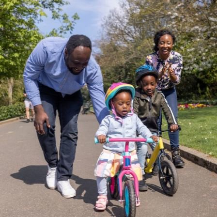 Family Teaching Children To Ride A Bike