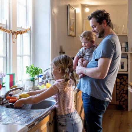 Father With Baby Watching Young Daughter With Chores