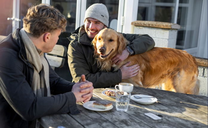 Two Men Talking At A Cafe With A Dog Landscape